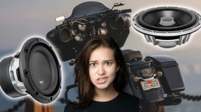 A lady in front of a large motorcycle with car audio speakers on each side, looking confused