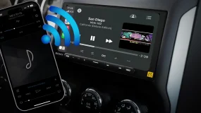 A cellphone with bluetooth bars coming out of it going towards a car audio radio screen